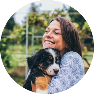 brown hair lady smiling while holding a bernese mountain dog puppy